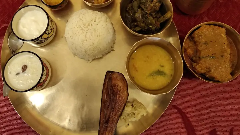 কাঁসার থালায় সাজানো ভাত, ডাল, বেগুন ভাজা, মাছের তরকারি আর দই