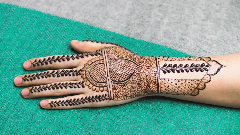 সবুজ কাপড়ের ওপর রাখা মেহেদির নকশা আঁকা একটি হাত