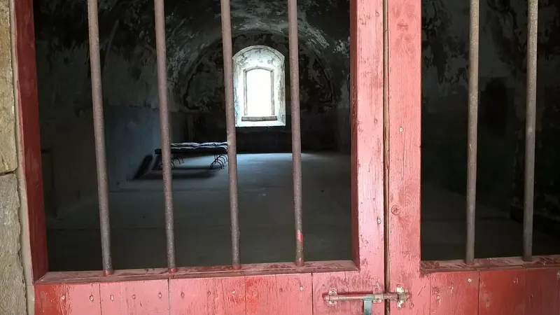 পুরনো কারাগারের লাল লোহার শিকের দরজার ওপারে ছোট জানালা দিয়ে আলো আসা একটি কুঠুরি