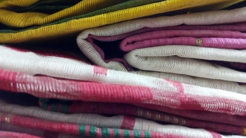 ভাঁজ করে স্তূপ করে রাখা হলুদ, সাদা আর গোলাপি রঙের কয়েকটি জামদানি শাড়ি