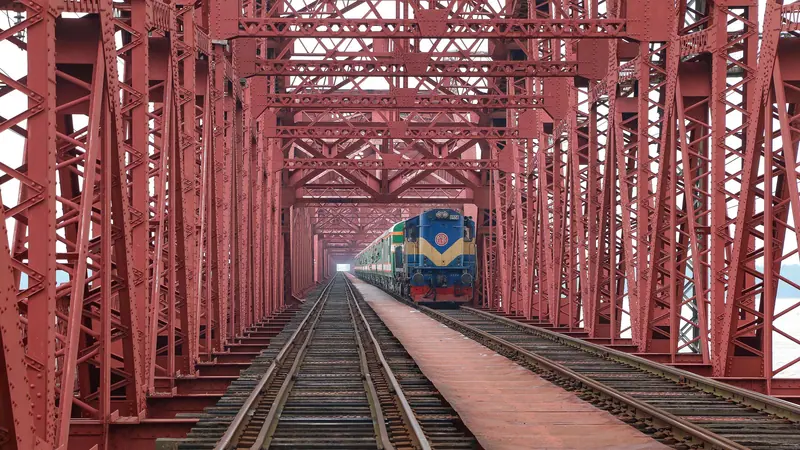 লাল লোহার সেতুর ভেতর দিয়ে এগিয়ে আসা একটি ট্রেন