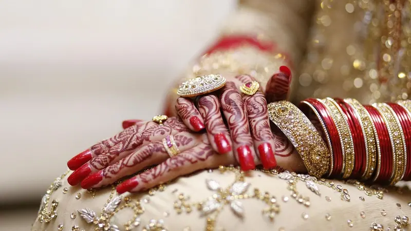 জরির কাজ করা বিয়ের পোশাকের ওপর রাখা কনের মেহেদি রাঙা দুই হাত, লাল আর সোনালি চুড়ি আর আংটি